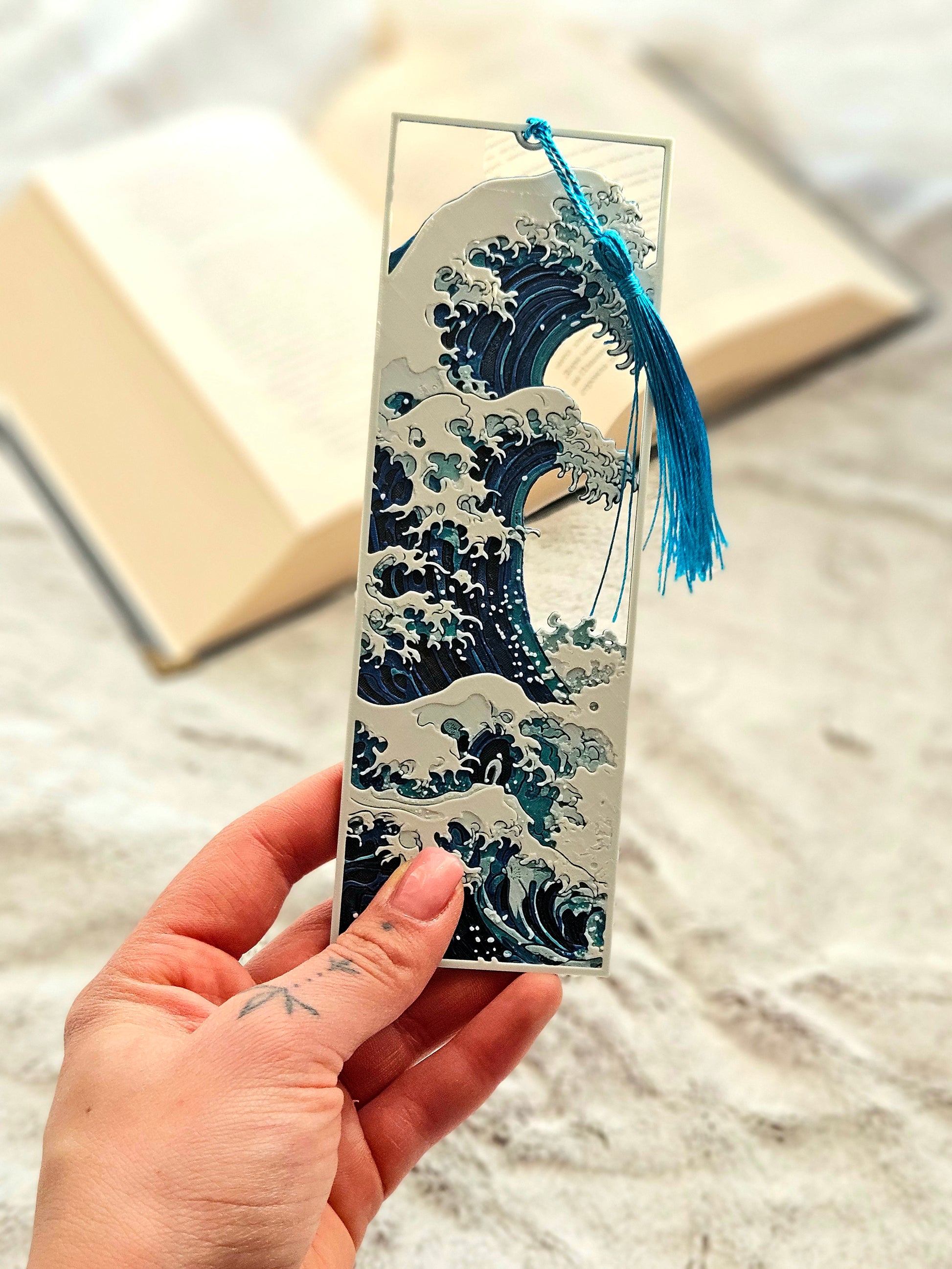 Hand holding a decorative bookmark with wave design and blue tassel.